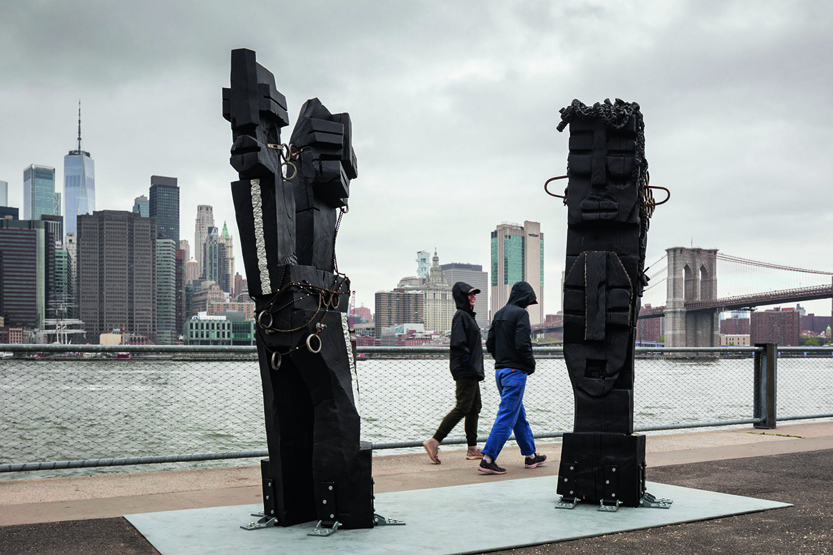 two people walking by a river passing two sculptures