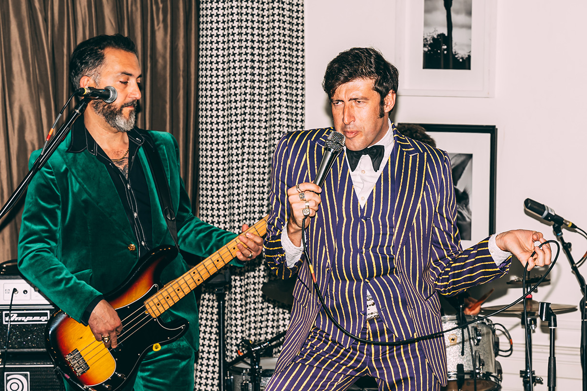 A man in a green suit playing guitar next to a man singing in a purple striped suit