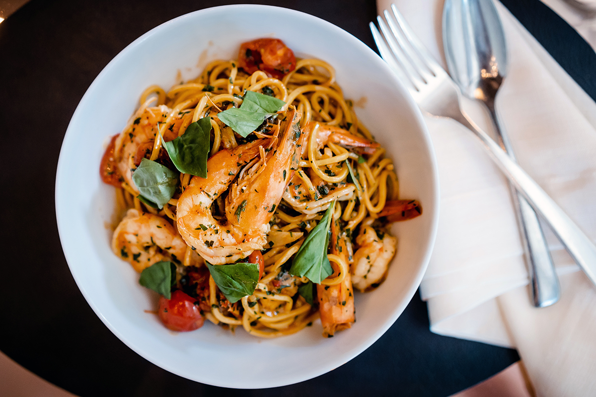 A bowl of tomato and basil pasta with prawns on top