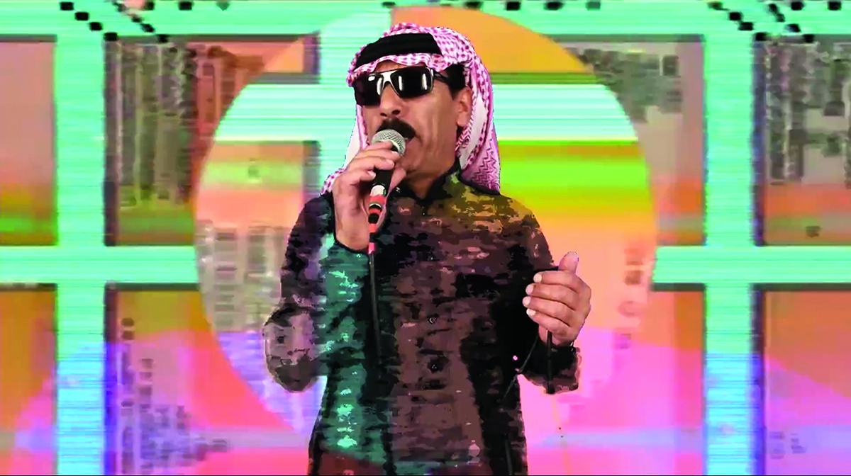 A man wearing an Arabic headscarf and brown dress holding a microphone