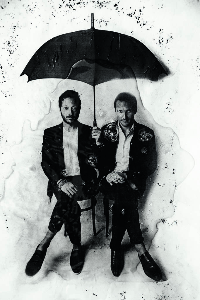 Two men in suits sitting under an umbrella
