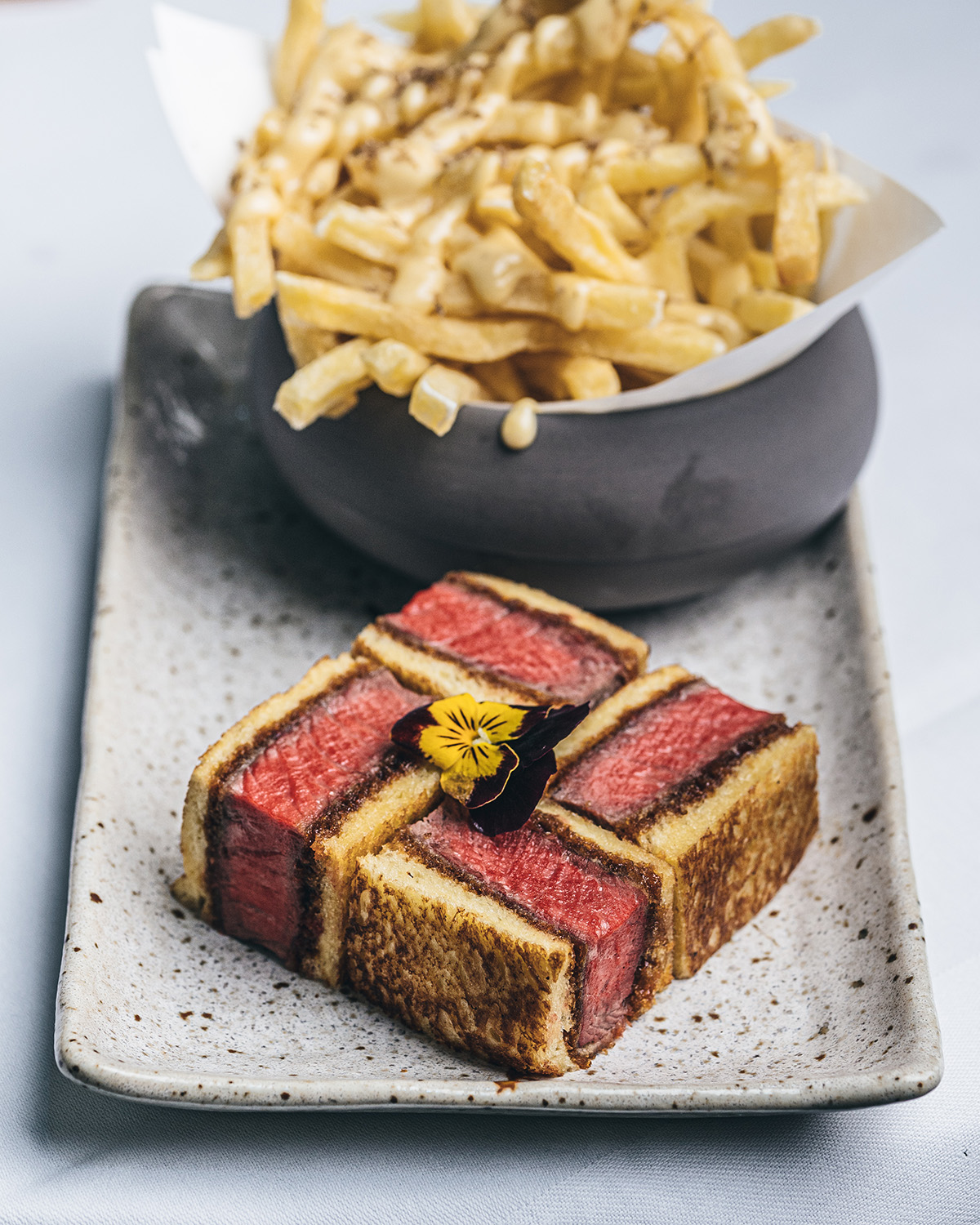 A cut up steak sandwich into a square with a bowl of french fries