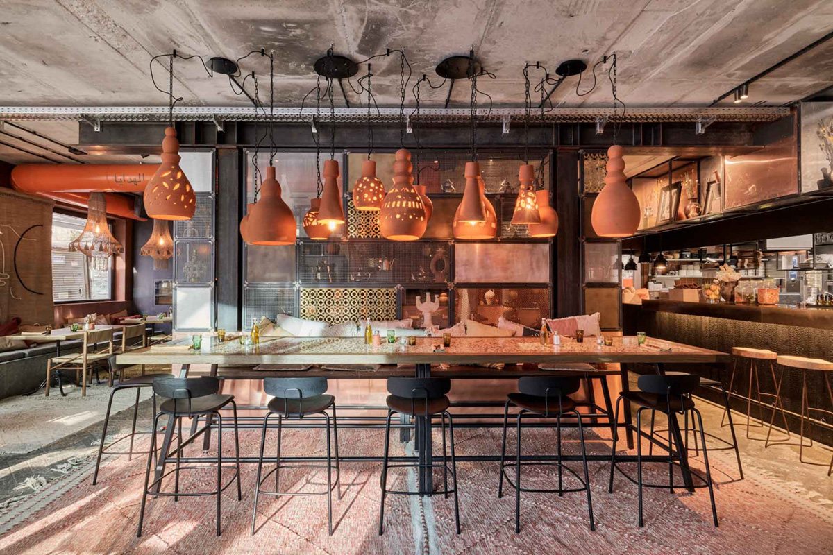 A restaurant with barstools and high tables and copper lamps hanging from the ceiling