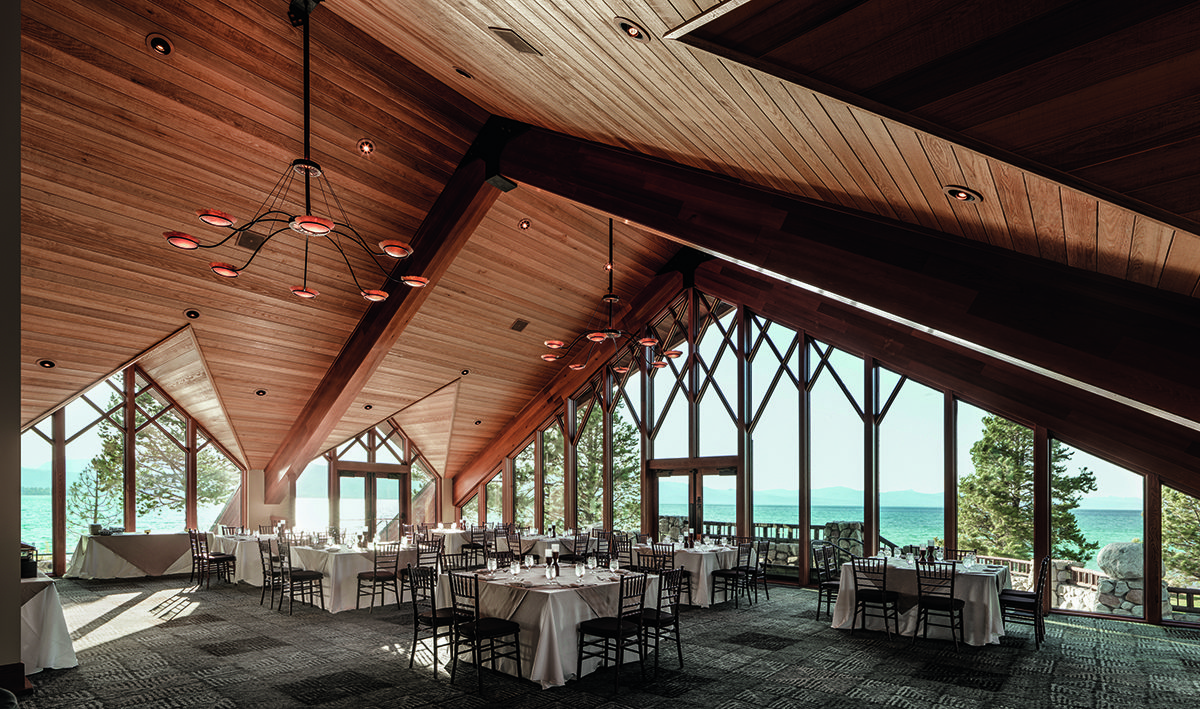 A wooden room with tables and chairs large windows 