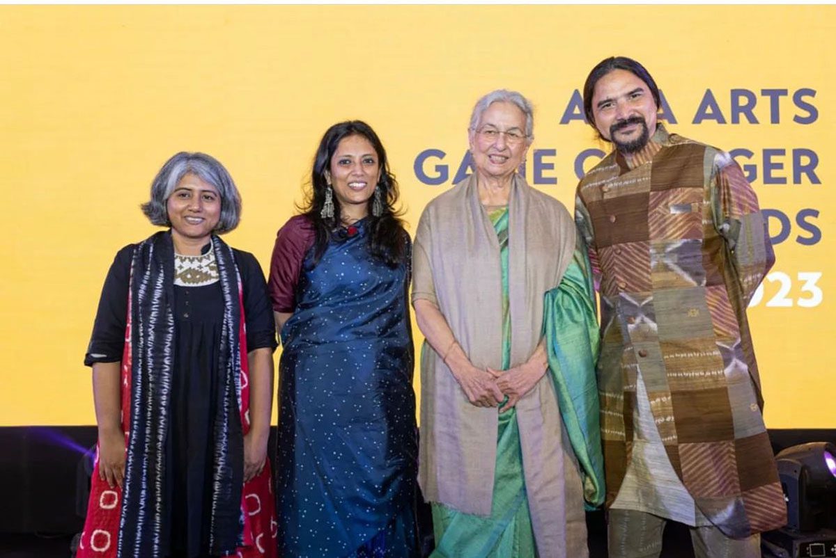 three women and a man all wearing dresses and tunics standing side by side