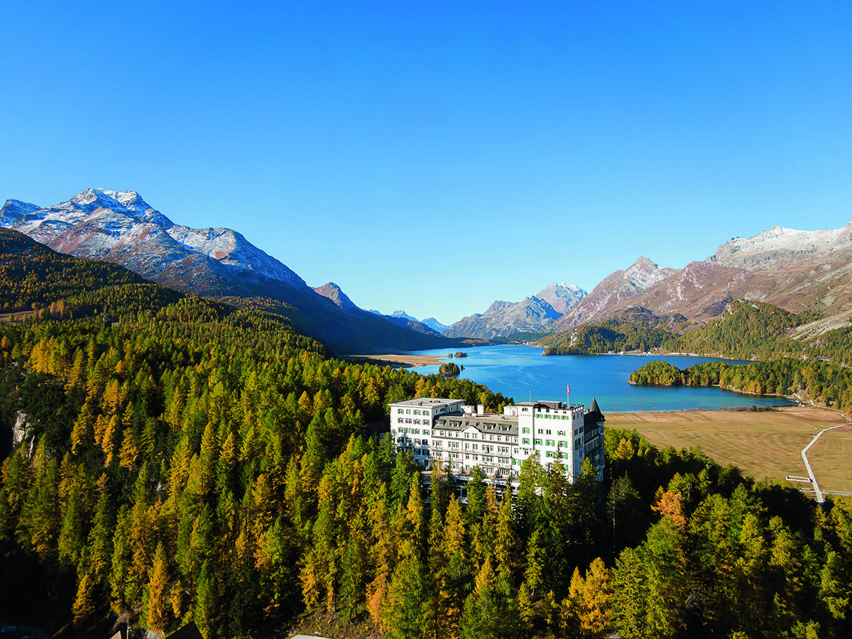 a hotel amongst trees and a lake and mountains in the background