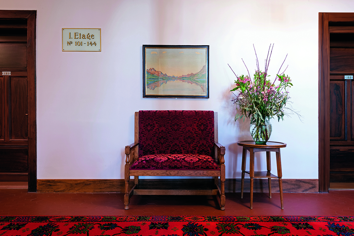 A red chair on a red carpet with a painting above it and a table with flowers next to it