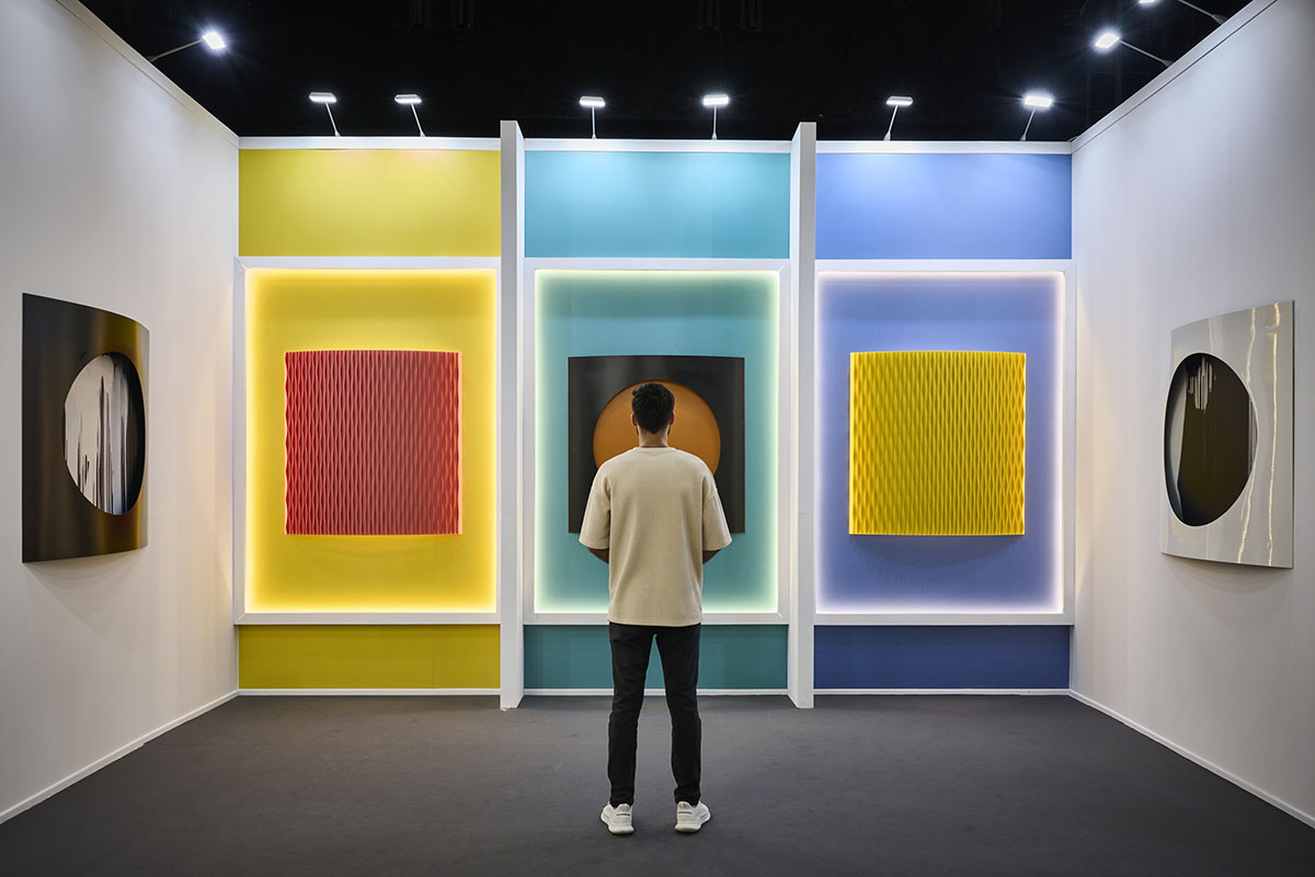 A man looking at three squares of art in blue, yellow and purple