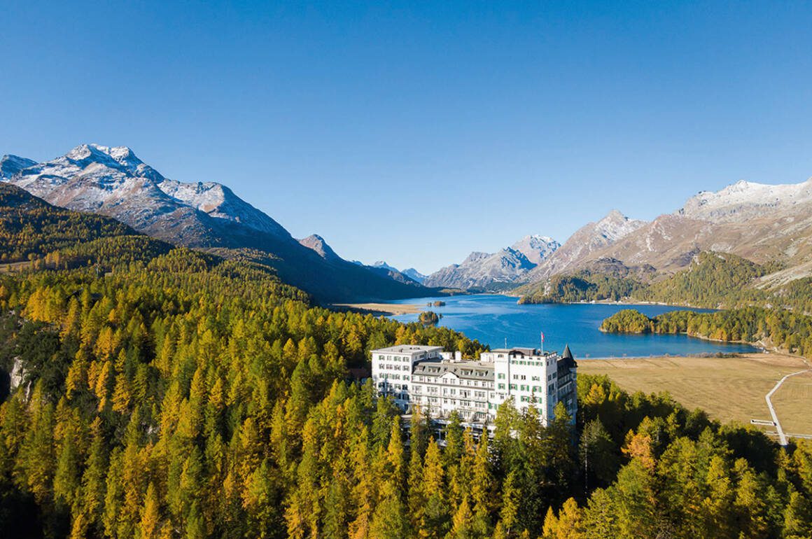 a hotel amongst trees and a lake and mountains in the background