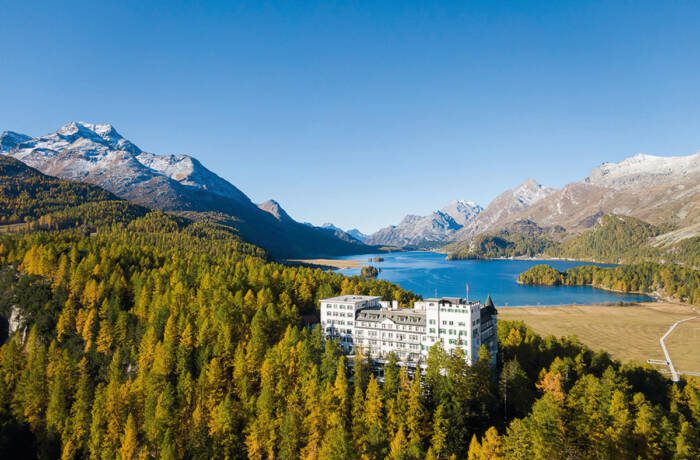 a hotel amongst trees and a lake and mountains in the background