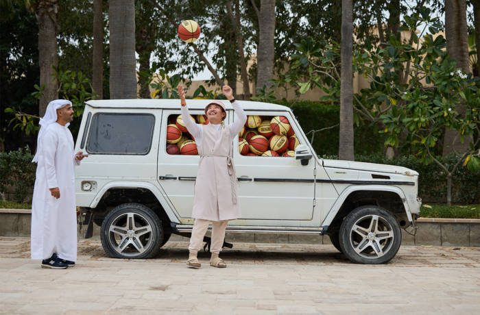 Two men playing with a basket ball standing next to a van filled with basket balls