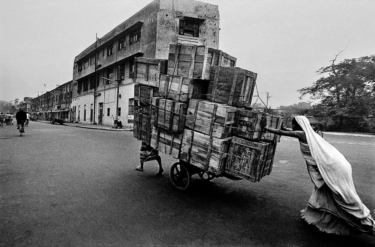 A woman pushing a heavy cart on a road