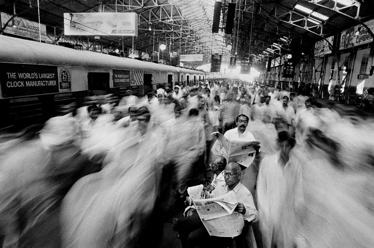 People moving in a station and a man reading a newspaper in the middle