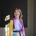 a woman smiling wearing a multicoloured dress with yellow sleeves