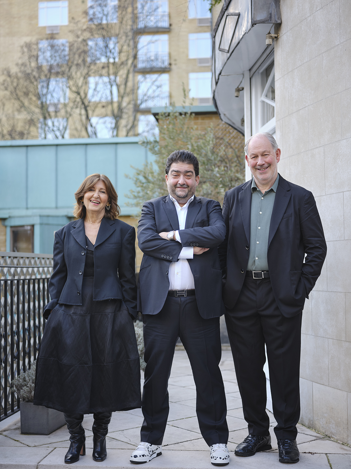 Two men and a woman all wearing dark suits standing side by side