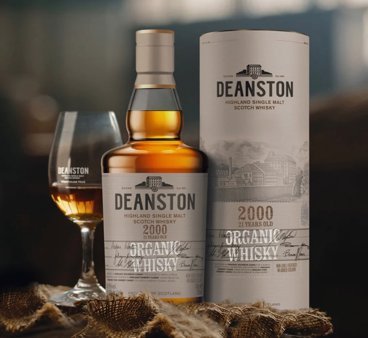 A glass of whiskey next to a bottle and case of Deanston Whiskey