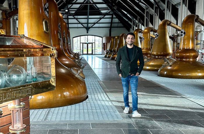 A man standing in a whiskey factory wearing jeand and a grey jacket