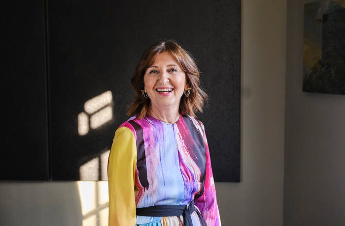 a woman smiling wearing a multicoloured dress with yellow sleeves