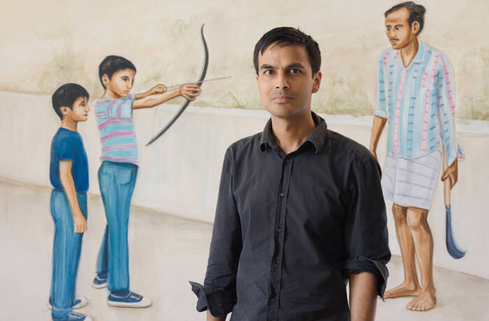 A man standing in front of a painting of a boy with a bow and arrow