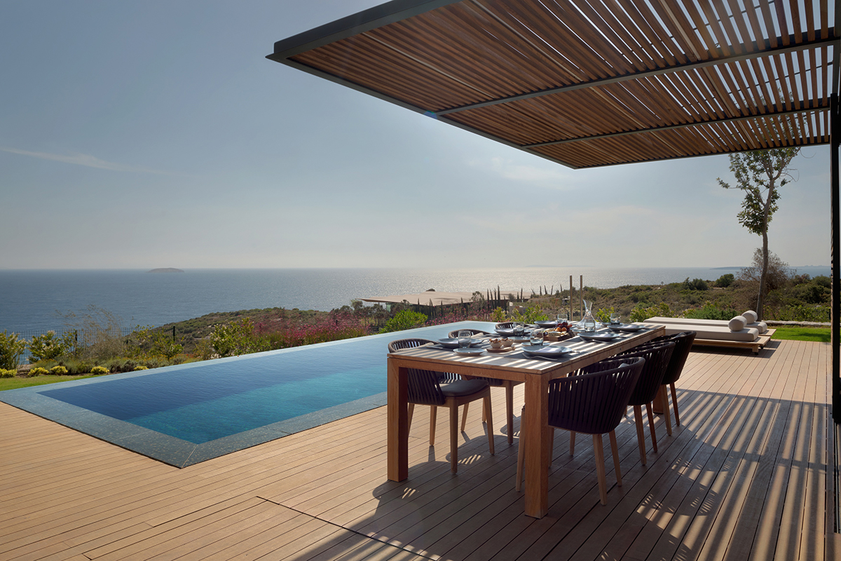 An infinity pool with a view of the sea and a terrace with a table and chairs