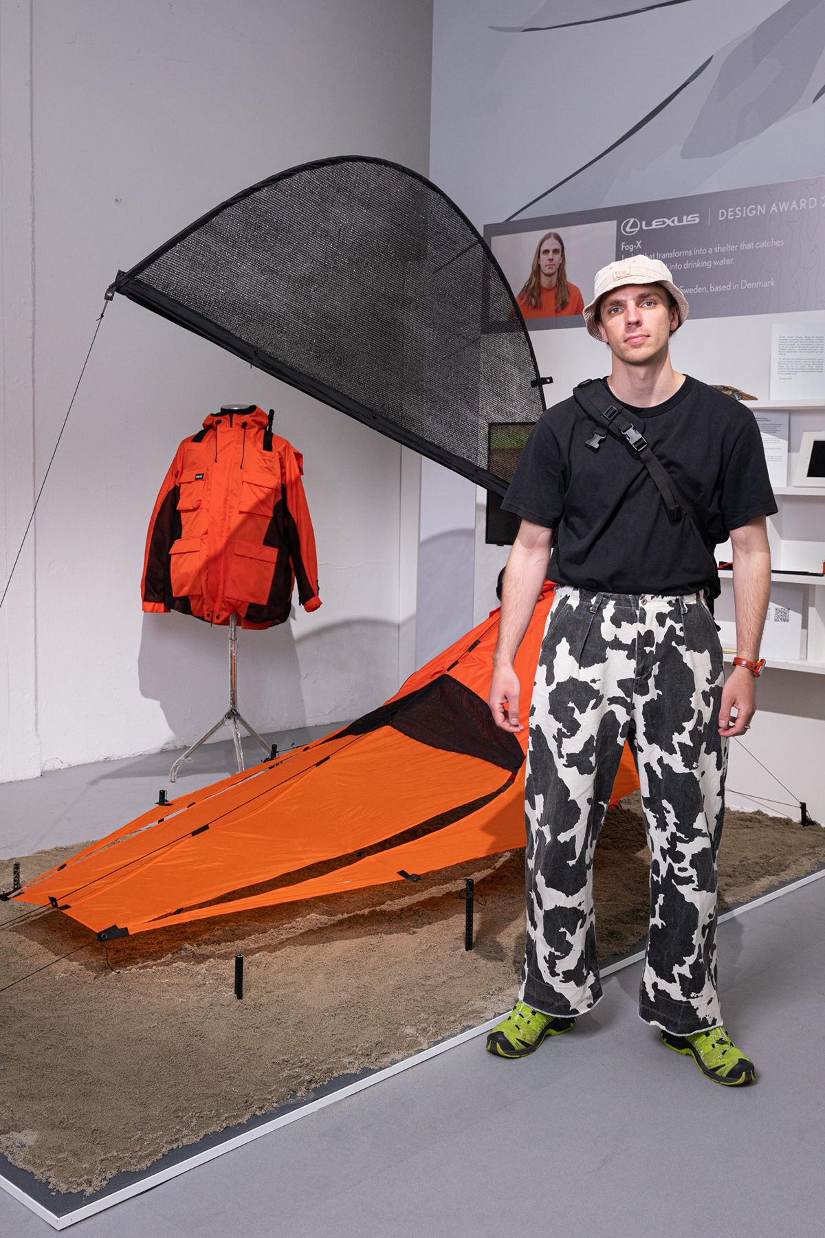 A man wearing cow print trousers and a black top standing next to an orange bag