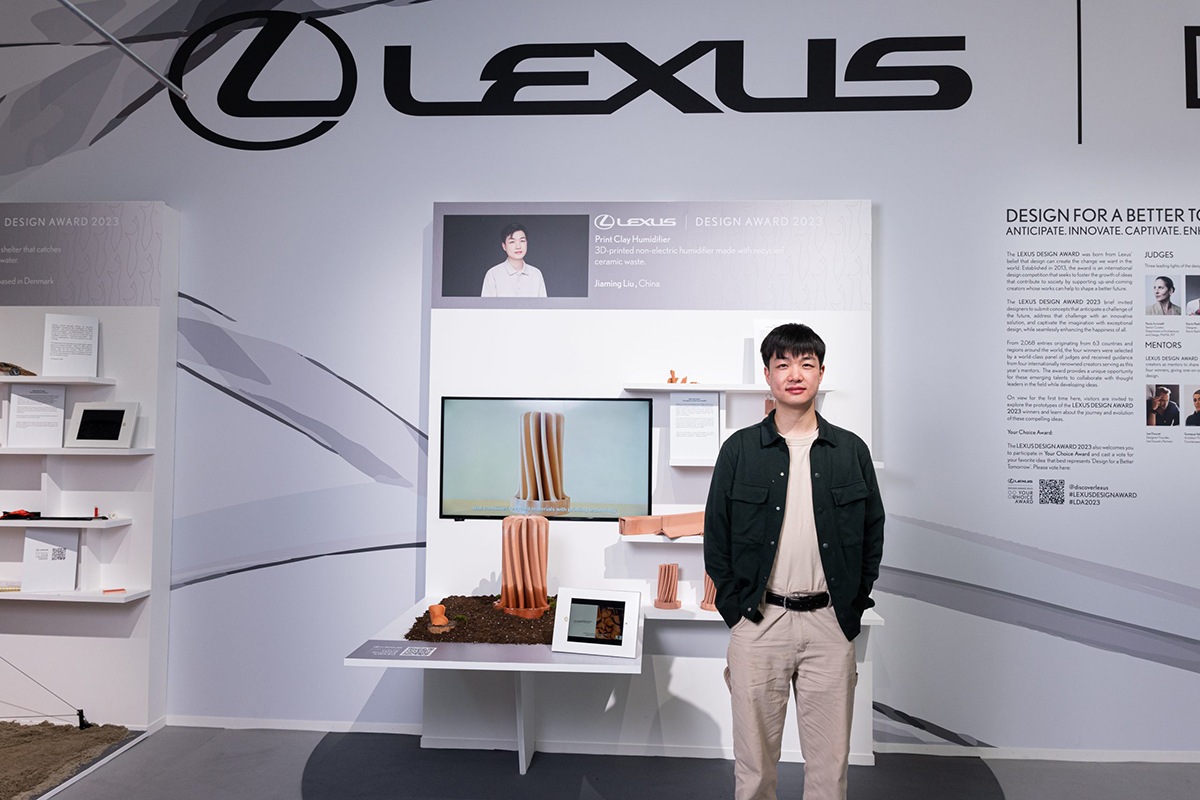 A man standing next to a product and a screen with the words LEXUS above him