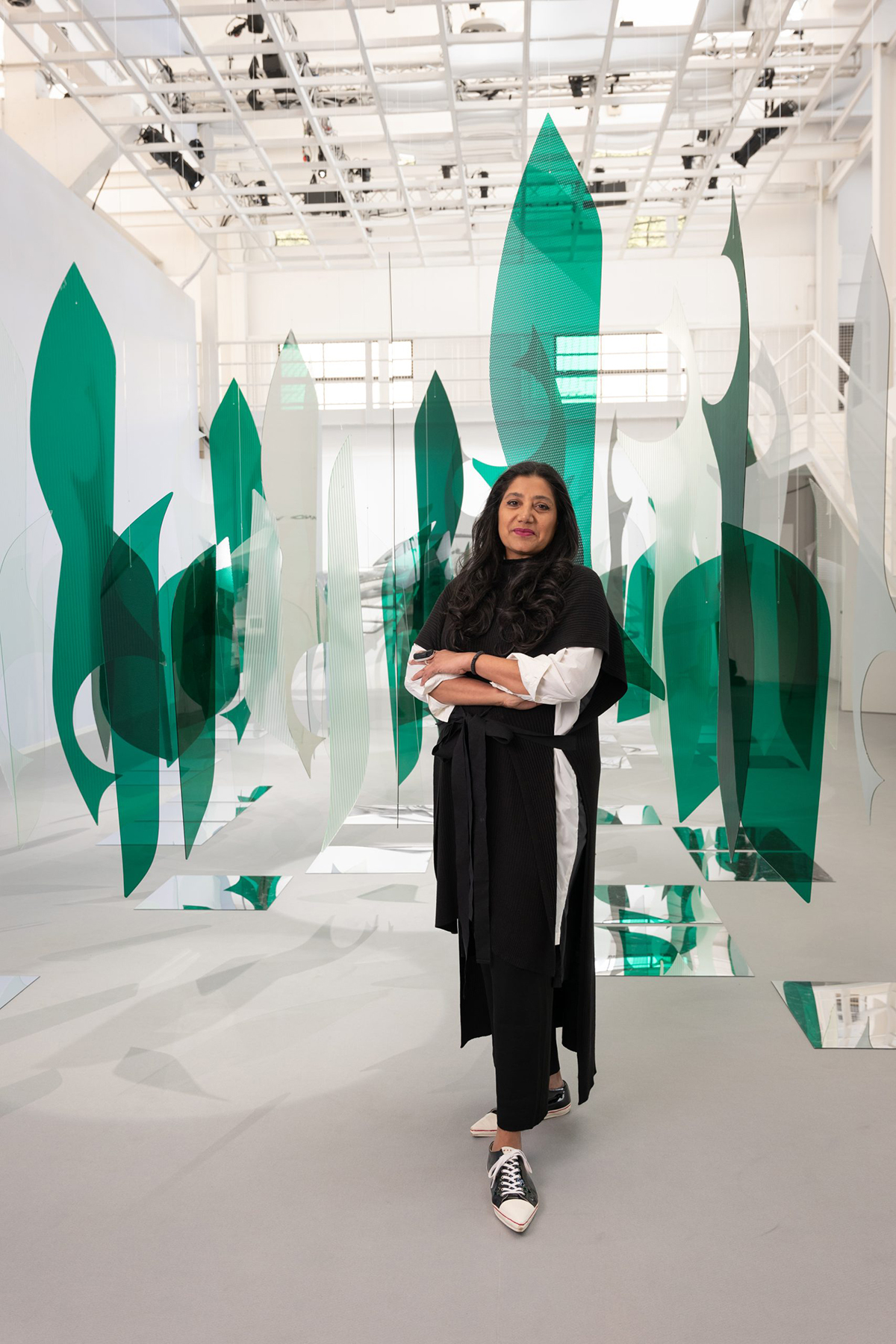 A woman wearing a black dress and white top standing next to green and transparent sheets of glass