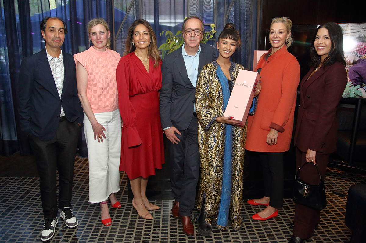 people standing together in different coloured outfits gathering for a photo with a pink champagne case