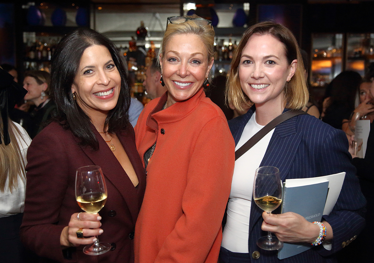 Three women standing together with two on either side holding champagne glasses