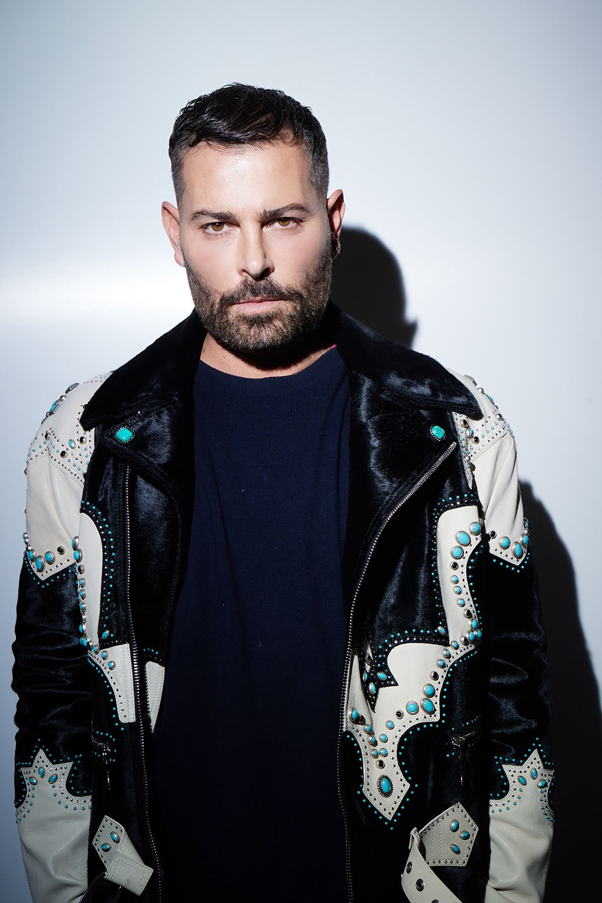 A man wearing a navy t-shirt and black and white jacket