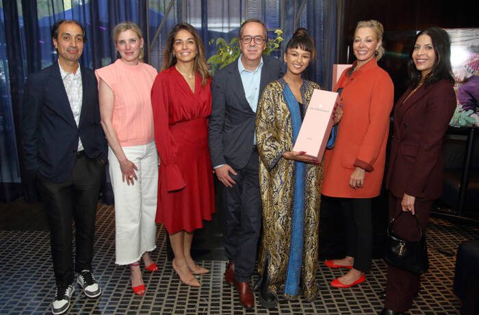 people standing together in different coloured outfits gathering for a photo with a pink champagne case