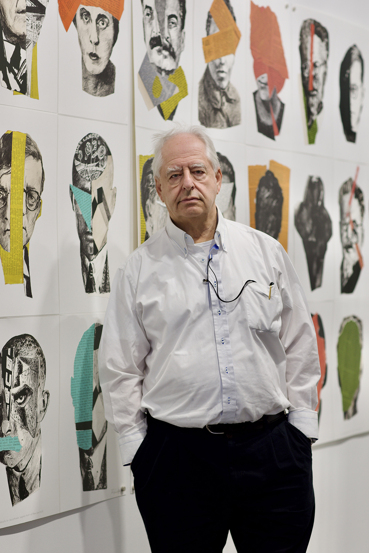 A man standing in a white shirt with his hands in his pockets in front of pieces of art on a wall