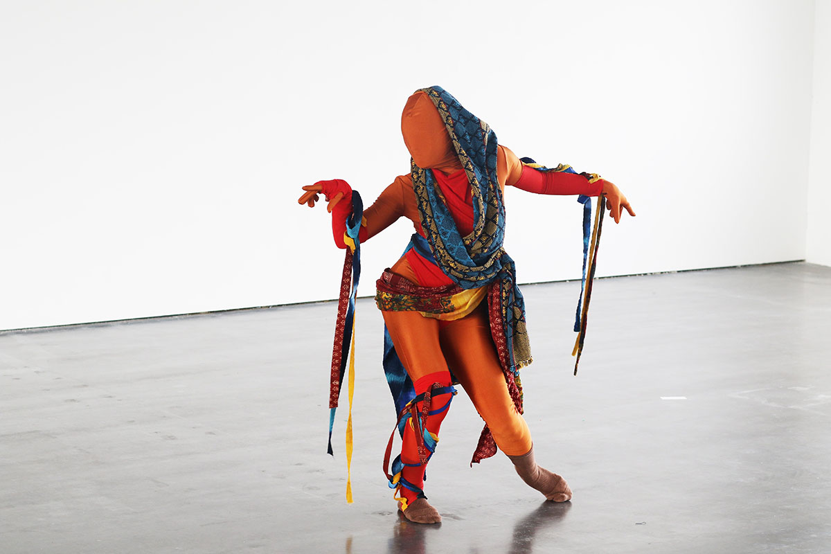 A person wearing an orange and blue string outfit with their face covered