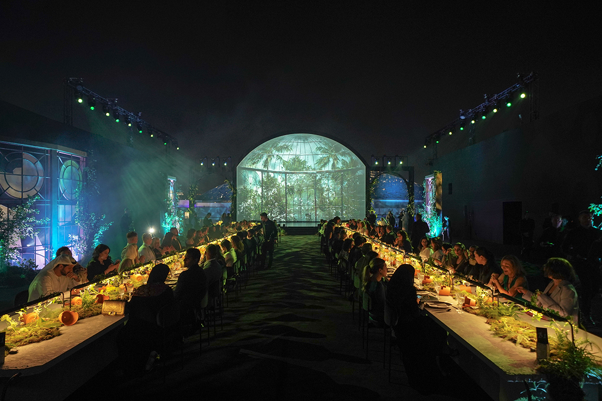 Two long tables in a room with a green light up sign for Richard Mille at the end of the room