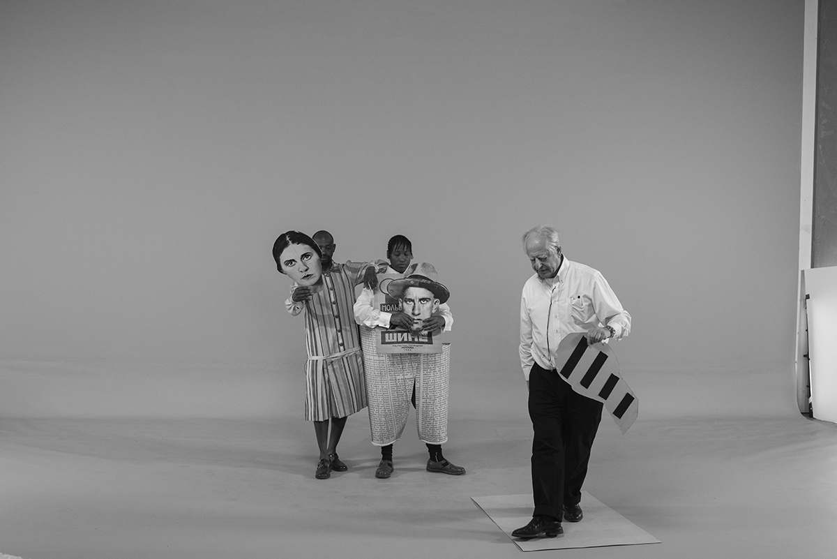 A man holding an instrument and two people in costumes holding giant heads watching him