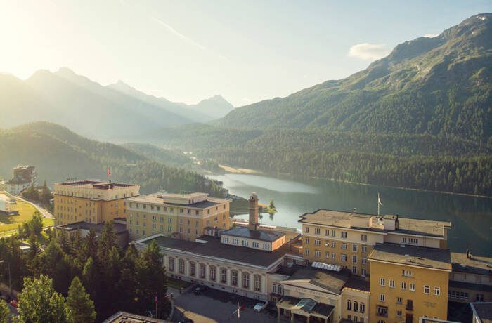 A yellow hotel with a lake and mountains behind it