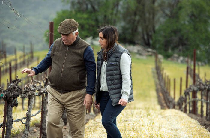 a man and woman walking in a vineyard