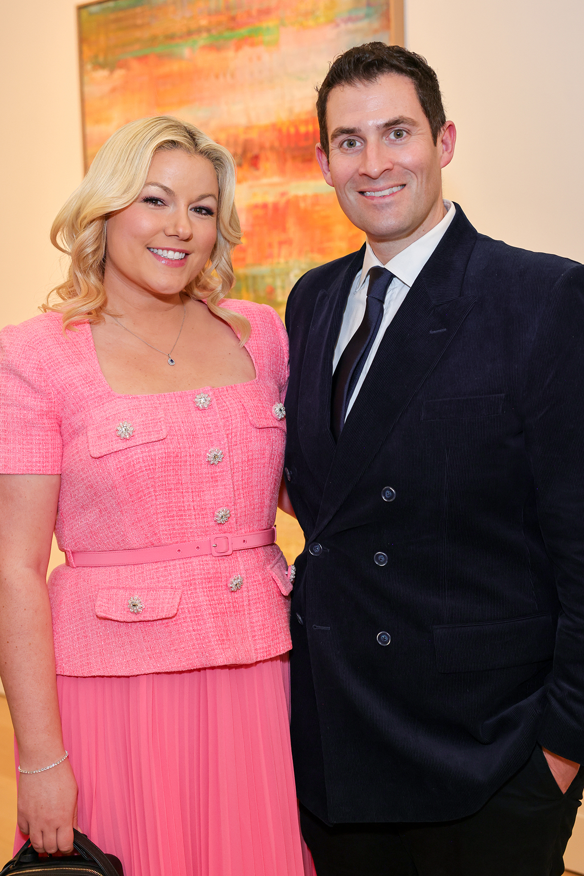 A blonde woman in a pink dress standing next to a man a black suit and tie with a white shirt