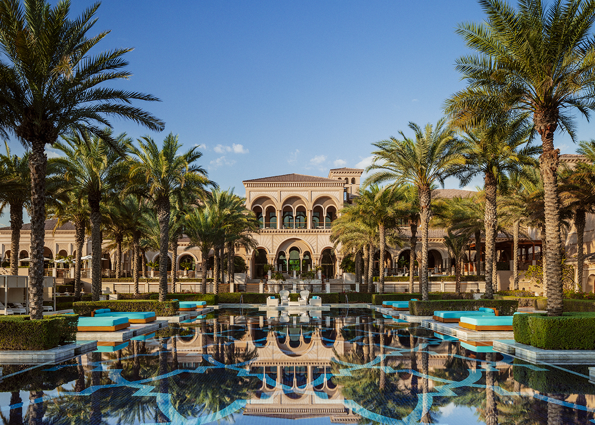 A palace surrounded by palm trees and a swimming pool at the front 