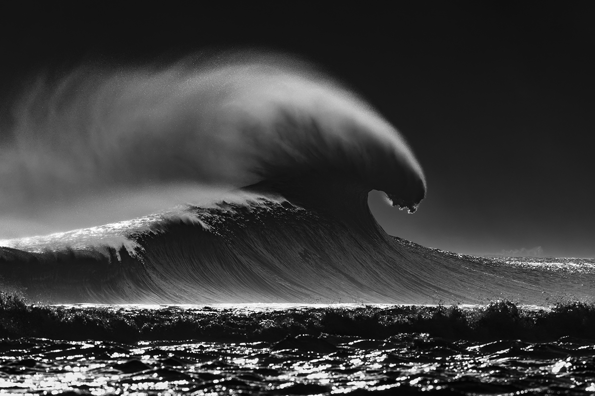 A black and white image of huge waves about to crash into the sea