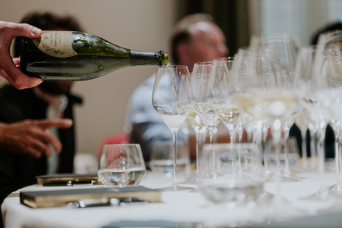 Someone pouring a green bottle of wine into a glass with a man sitting at the table