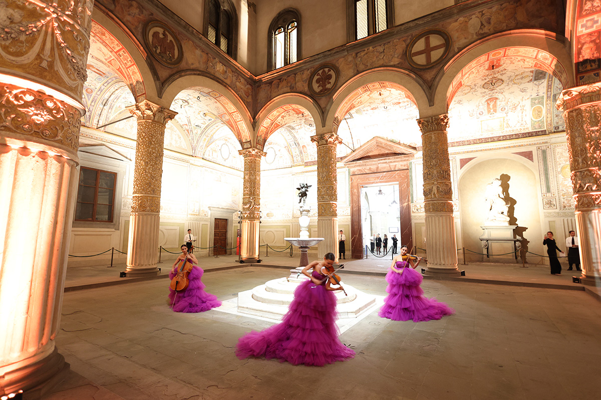 women in purple dresses playing violins outside an old Italian building in a courtyard