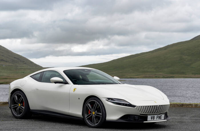 A white Ferrari by a river and hills