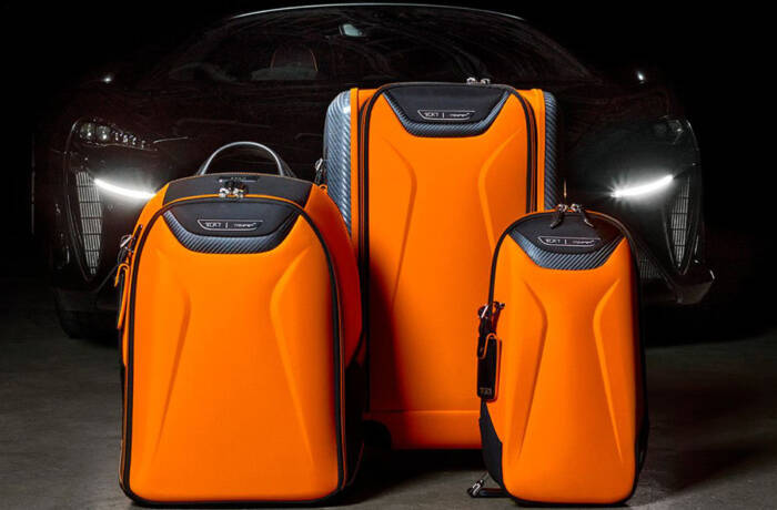 orange suitcases and rucksack in front of a black sportscar