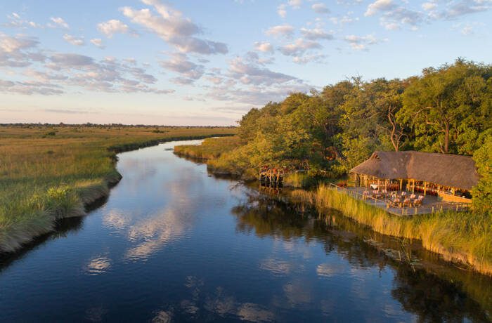 Wide glassy river bank surrounded by trees below a twilight sky