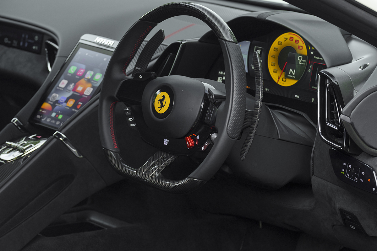a Ferrari steering wheel and controls in the Roma with the yellow Ferrari logo in the middle of the steering wheel