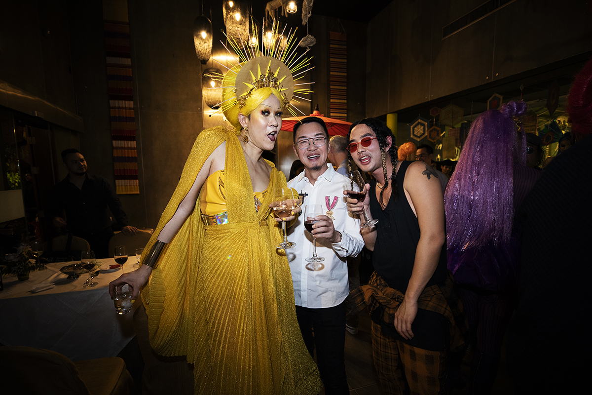 A woman wearing a gold dress and crown standing with two other people