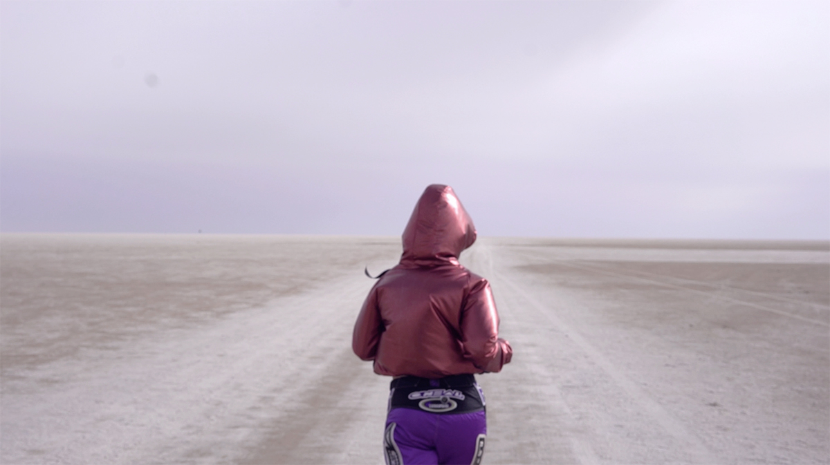 A woman running on an open path wearing a red jacket and purple bottoms