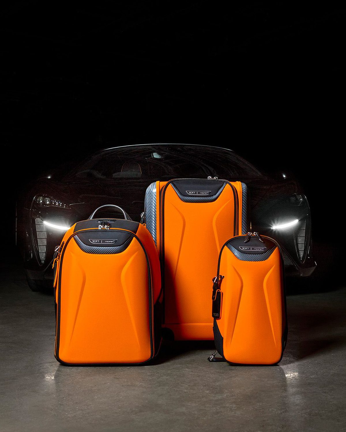 orange suitcases and rucksack in front of a black sportscar