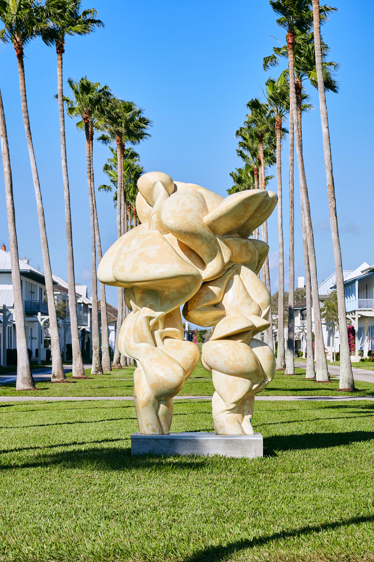 A beige statue on grass with palm trees around it